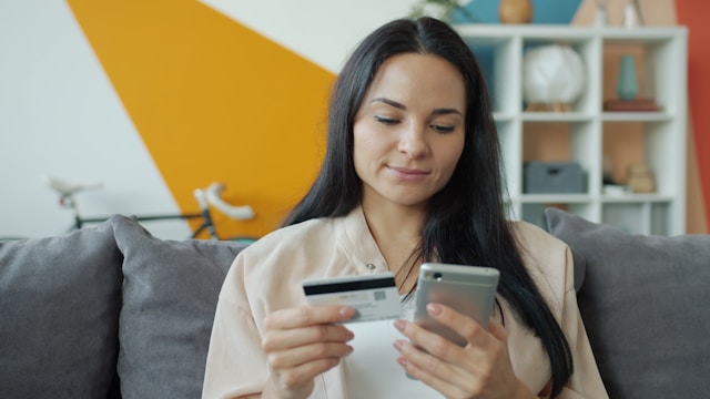 A person holding a card while using a phone, representing online checkout and trust.